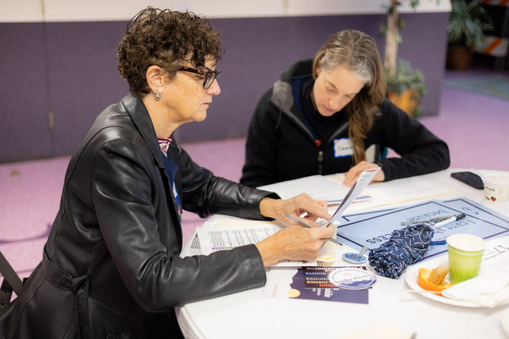 Two volunteers at a table with signs and brochures.