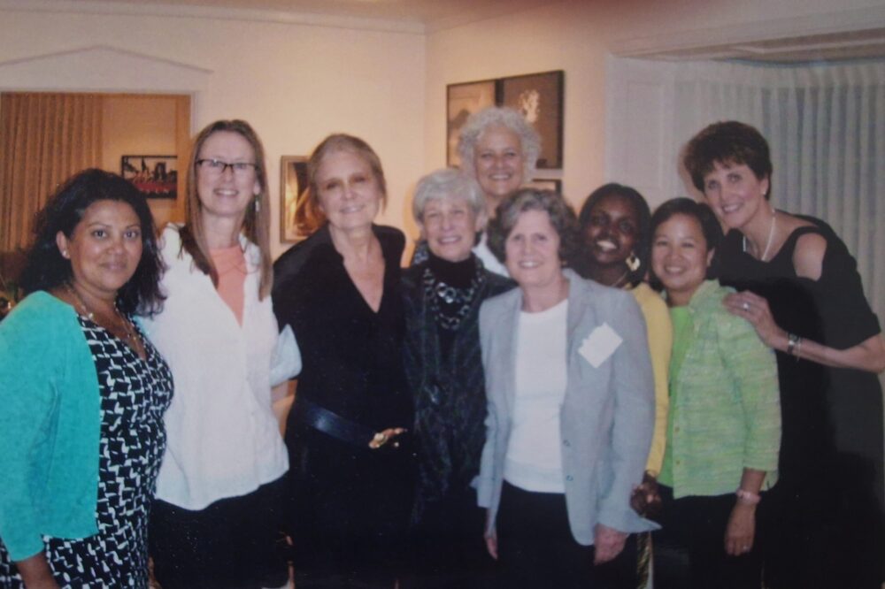 A group of women standing together in a room in the center Gloria Steinem