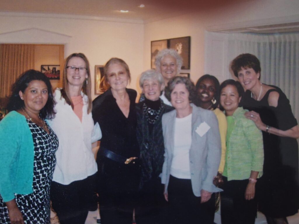 A group of women standing together in a room in the center Gloria Steinem