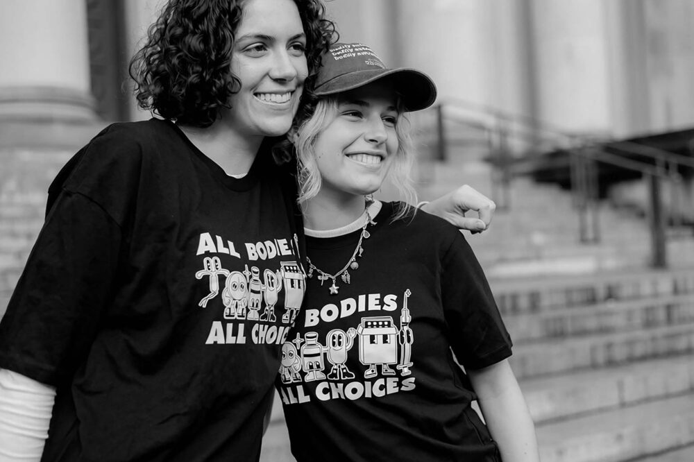 Two volunteers wearing "All Bodies All Choices" t-shirts